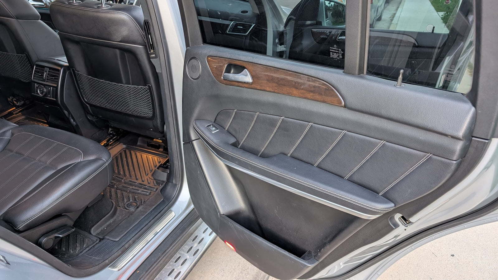 Luxury SUV's rear passenger area: black leather seats, wood trim, door open. A comfortable ride, unlike an rv rental.