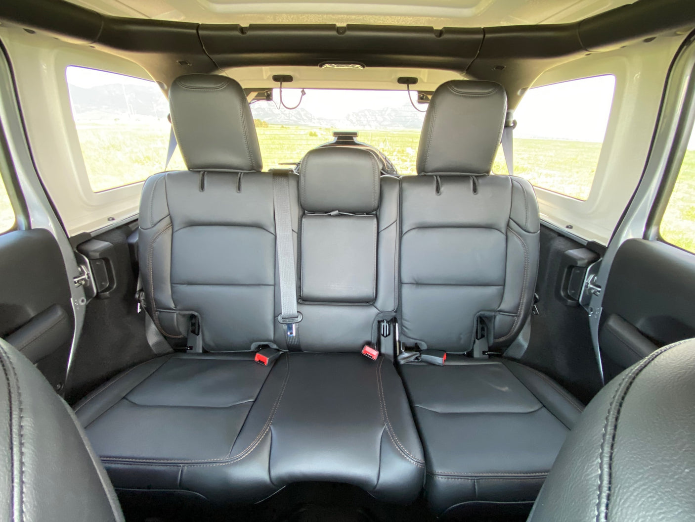 Interior of an SUV-style RV rental: black leather back seats, headrests, and scenic views of fields and mountains.