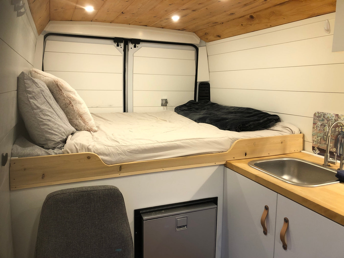 Experience comfort in this RV rental van conversion, featuring a bed, kitchen sink, and compact fridge.