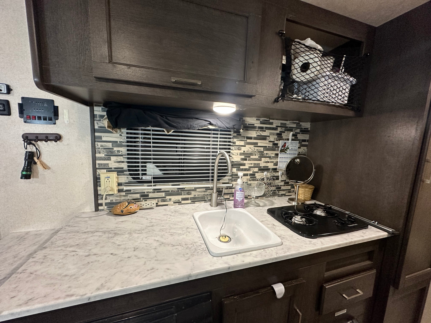 Inside an RV rental: a compact kitchen with sink, two-burner stove, and overhead storage.
