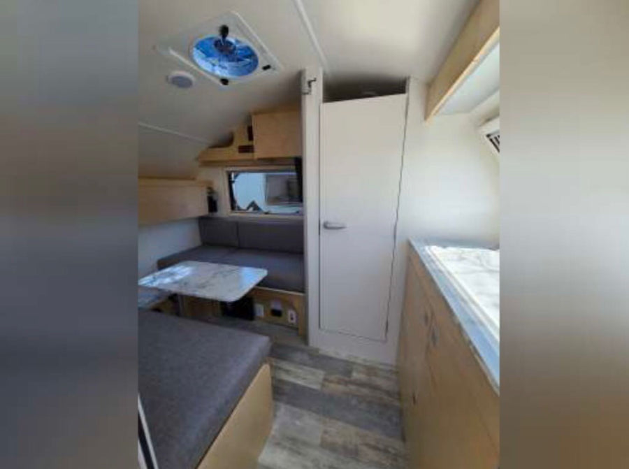 safely secured by a yellow chock block on asphalt.|View inside a modern RV rental featuring an L-shaped sofa