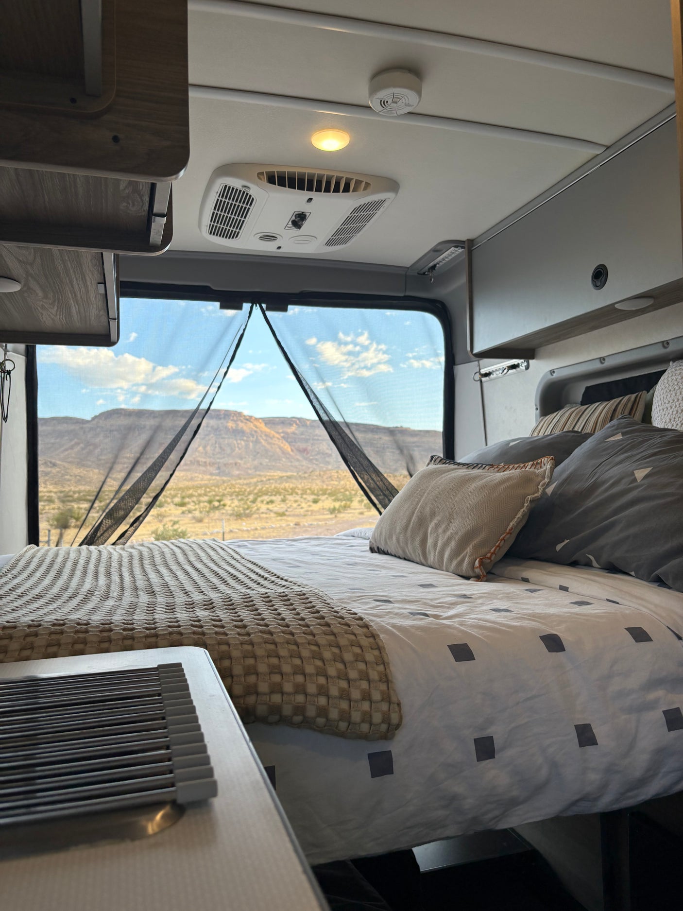 This inviting RV rental features a comfortable bedroom with panoramic desert mountain views, AC, and amenities for your road trip comfort.