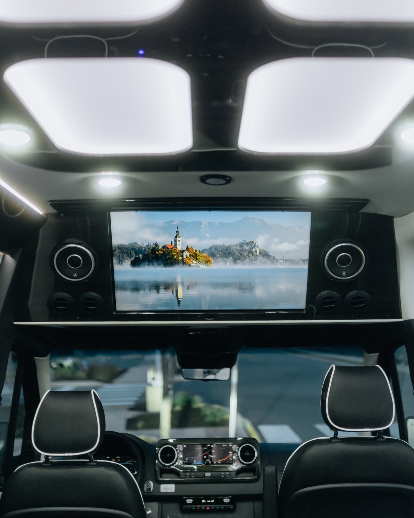 RV rental interior with large screen displaying scenic lake. Modern lighting and comfortable front seats visible.