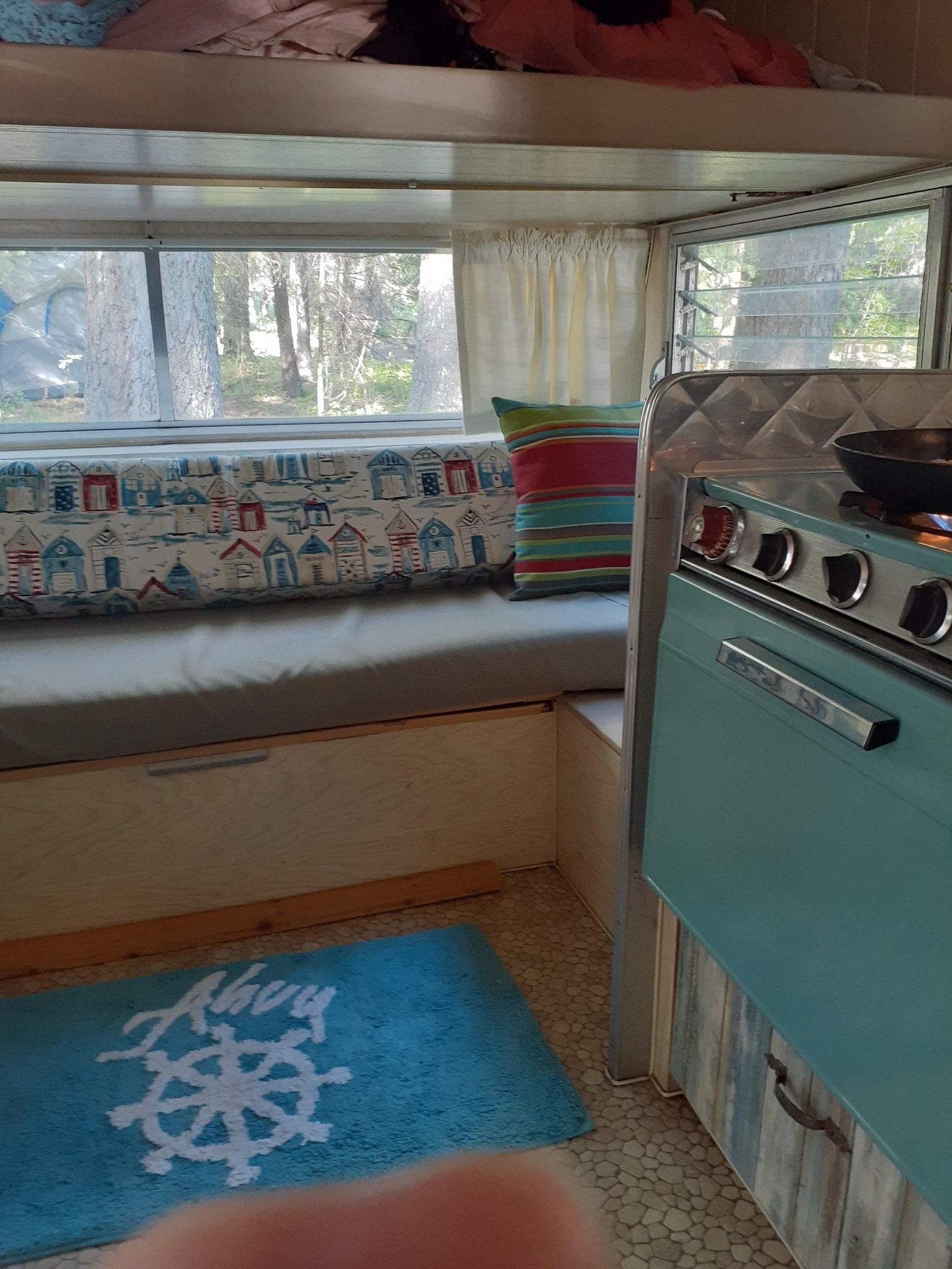 Enjoy this charming rv rental interior featuring a bunk, beach hut seating, and a retro blue stove, ideal for your next camping adventure.