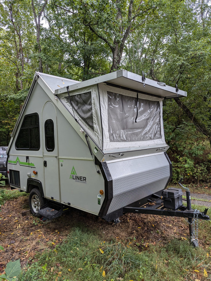This A-Liner A-frame RV rental is ready for camping, parked among trees in a serene outdoor setting.