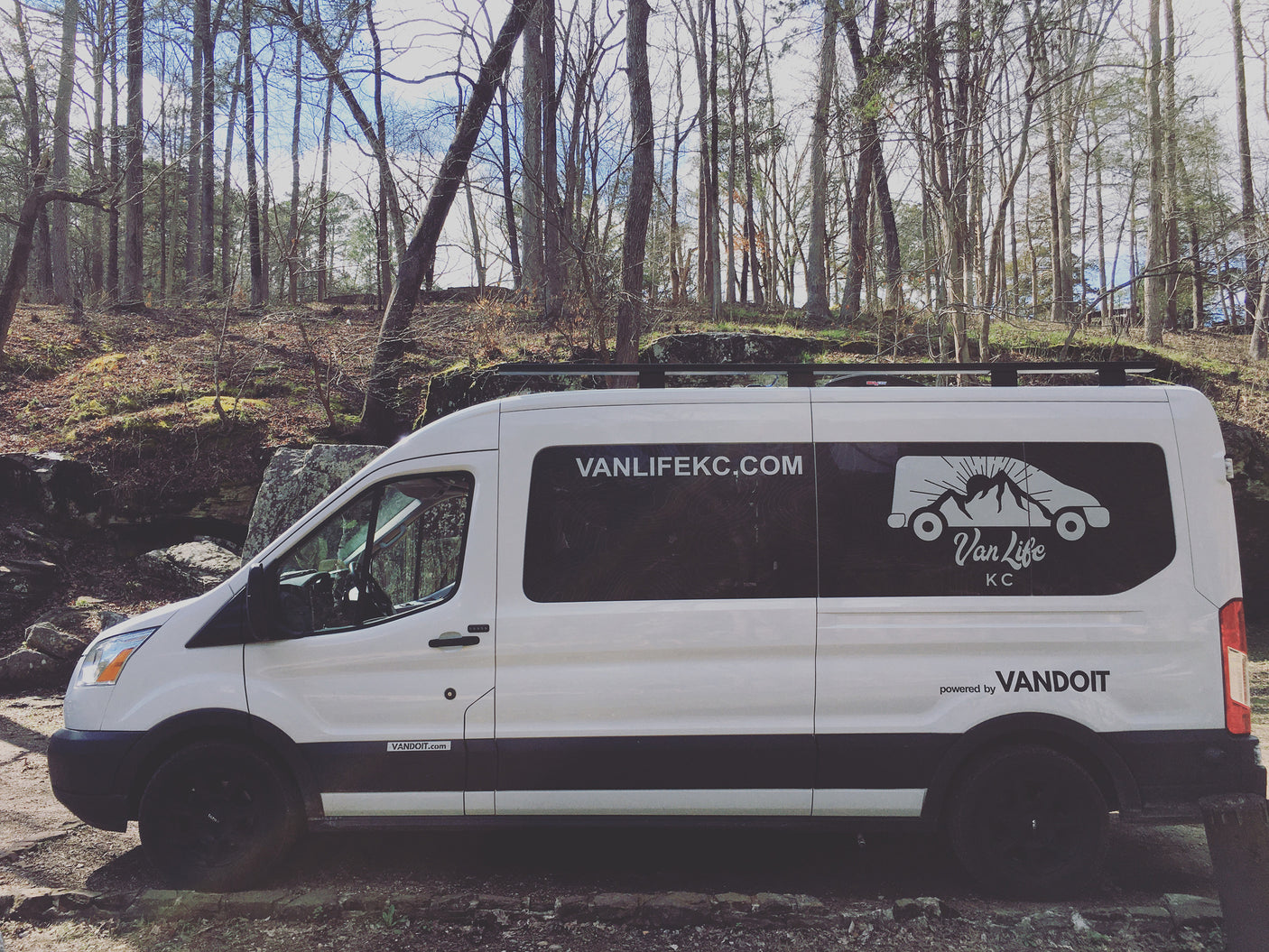 White Van Life KC RV rental van in a bare-treed forest with rocky ground. Perfect for your next adventure.