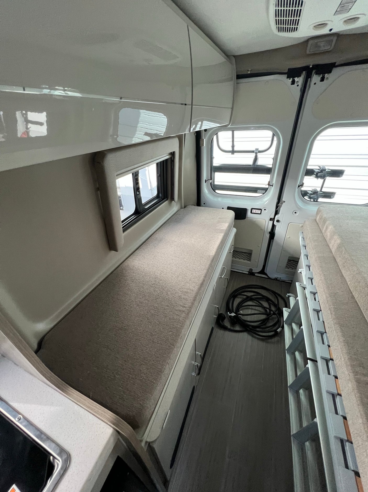 Efficient RV rental interior showcasing a comfortable bench bed, overhead storage, and accessible rear doors for camper van travels.