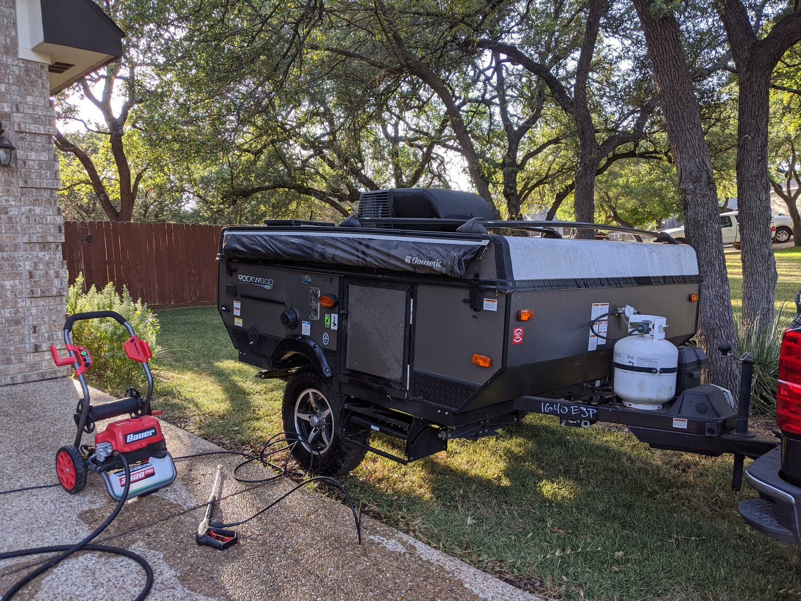 A dark gray Rockwood pop-up camper is being pressure washed for an RV rental service.