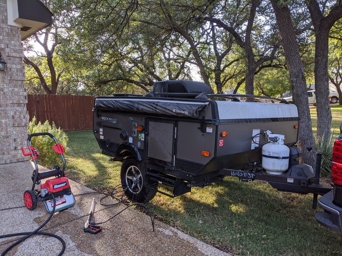 A dark gray Rockwood pop-up camper is being pressure washed for an RV rental service.