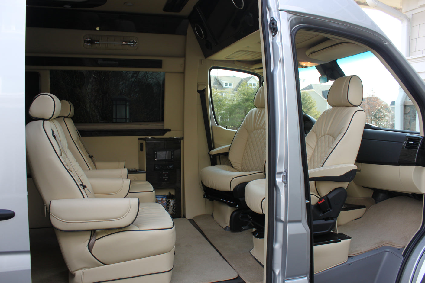 Luxury **rv rental** interior: comfortable cream leather captain's chairs, black piping, and entertainment console for premium travel.