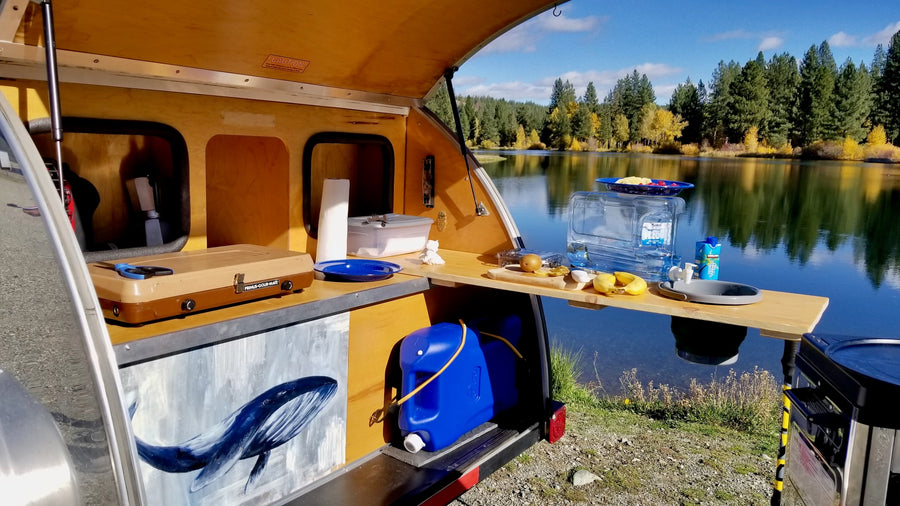 set by a scenic lake and mountains.|Enjoy nature with this RV rental! A shiny teardrop trailer by a lake