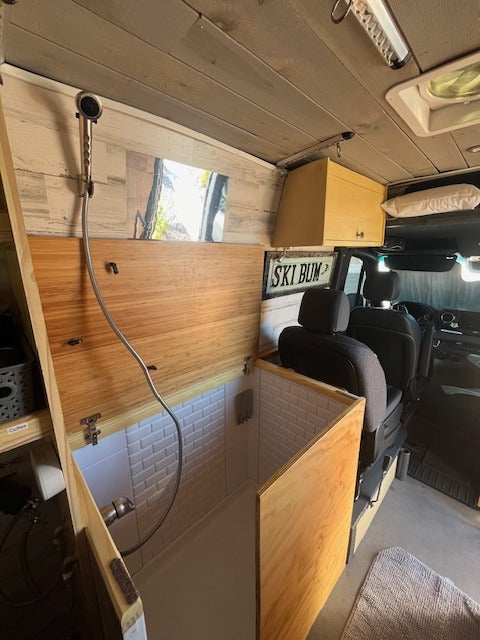 This RV rental showcases a compact, built-in shower with white subway tiles and wood paneling, perfect for mobile bathroom convenience.