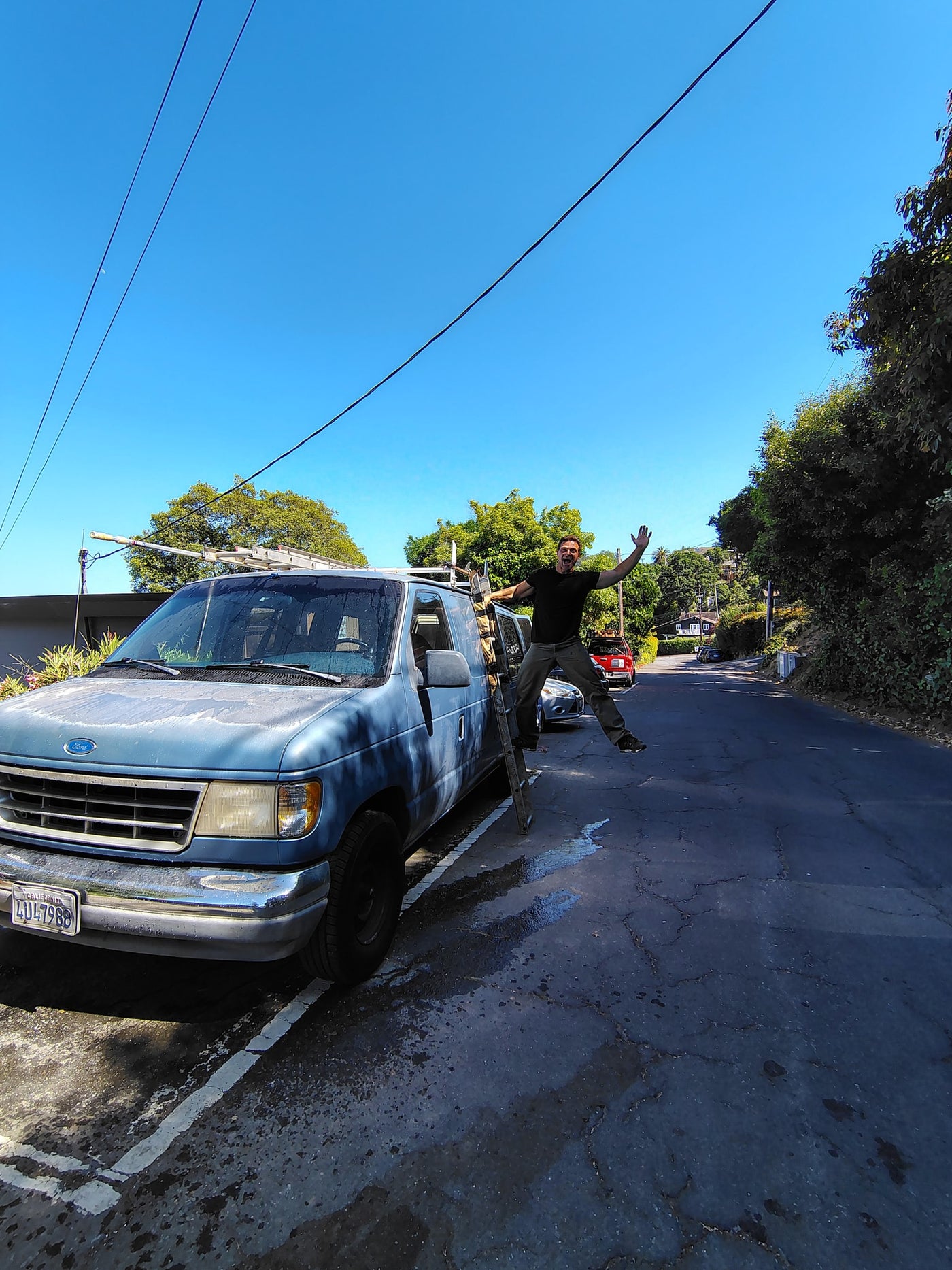 Joyful man leaps from blue work van on a sunny street, dreaming of an RV rental escape. — photo 5