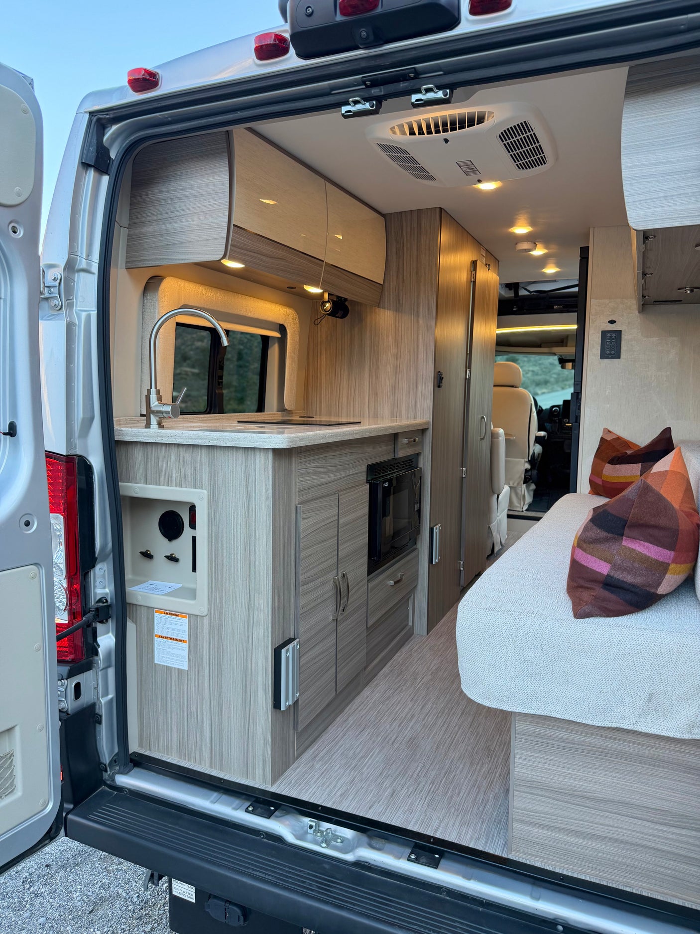 RV rental interior, showing kitchen, sink, microwave, and lounge seating from the open rear doors.