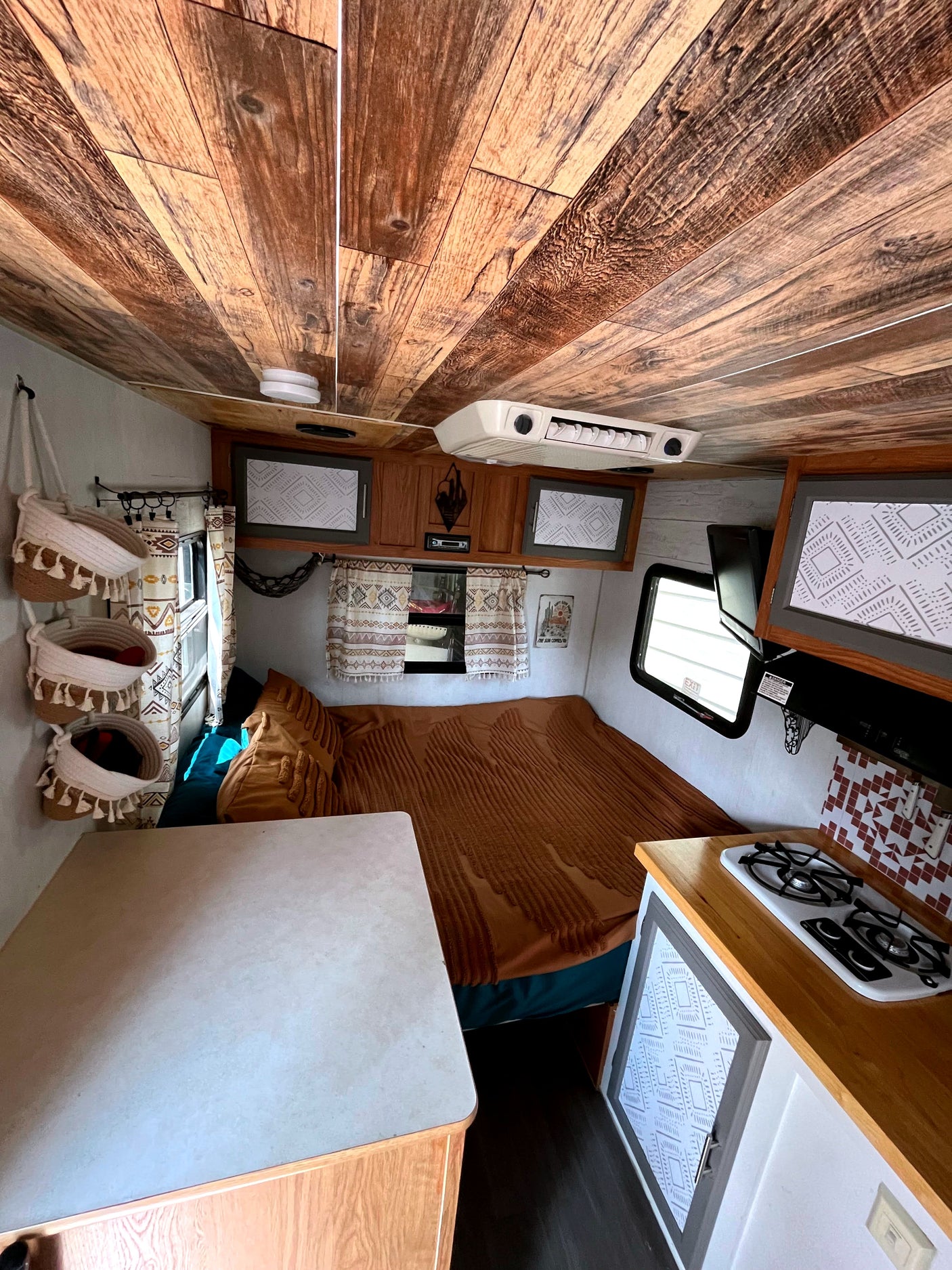Step inside this cozy RV rental! Features a rustic wood ceiling, comfortable bed, and compact kitchen.