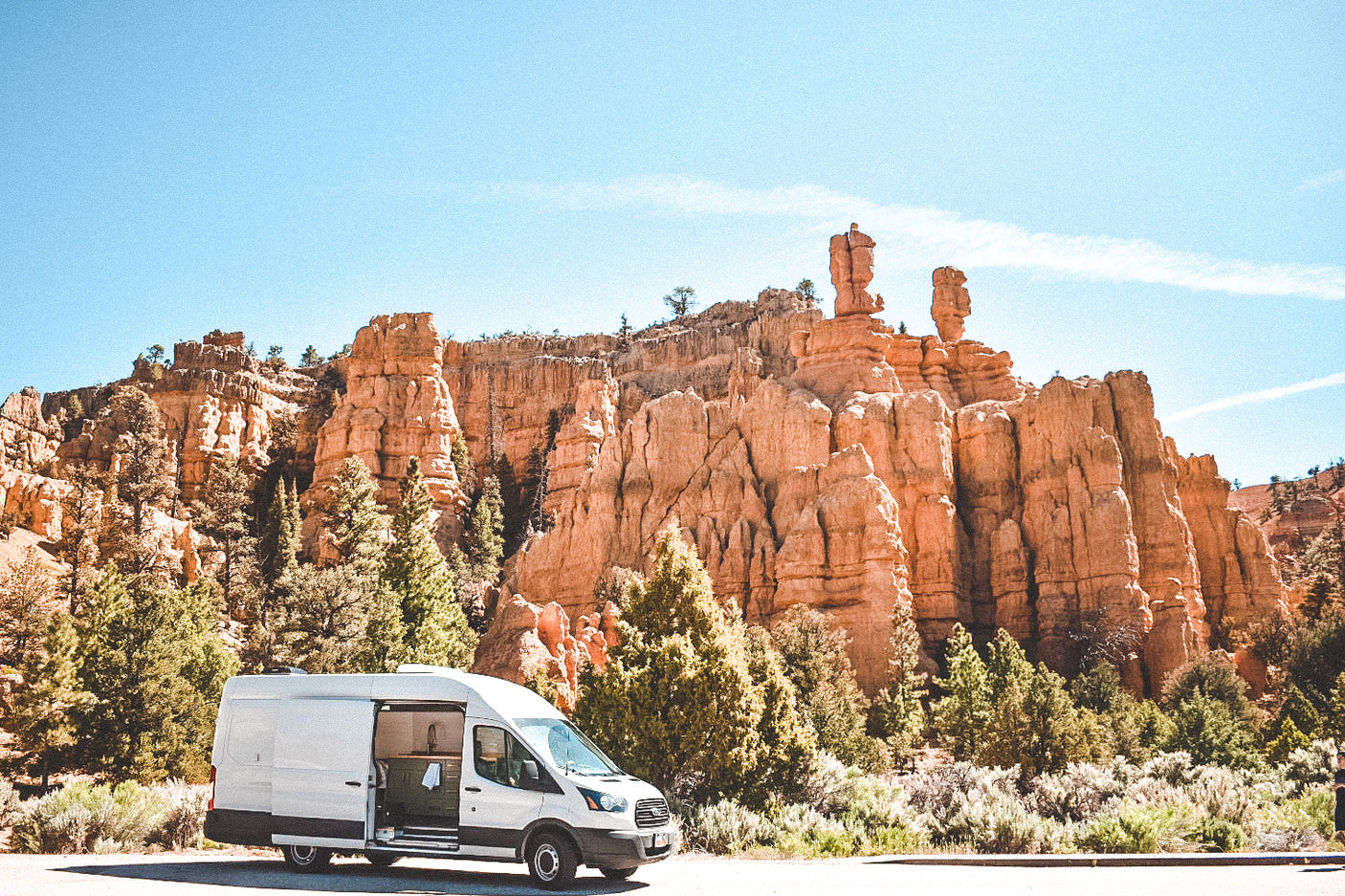 RV rental van at scenic red rock canyon under blue sky with trees. Ideal for adventure & van life.