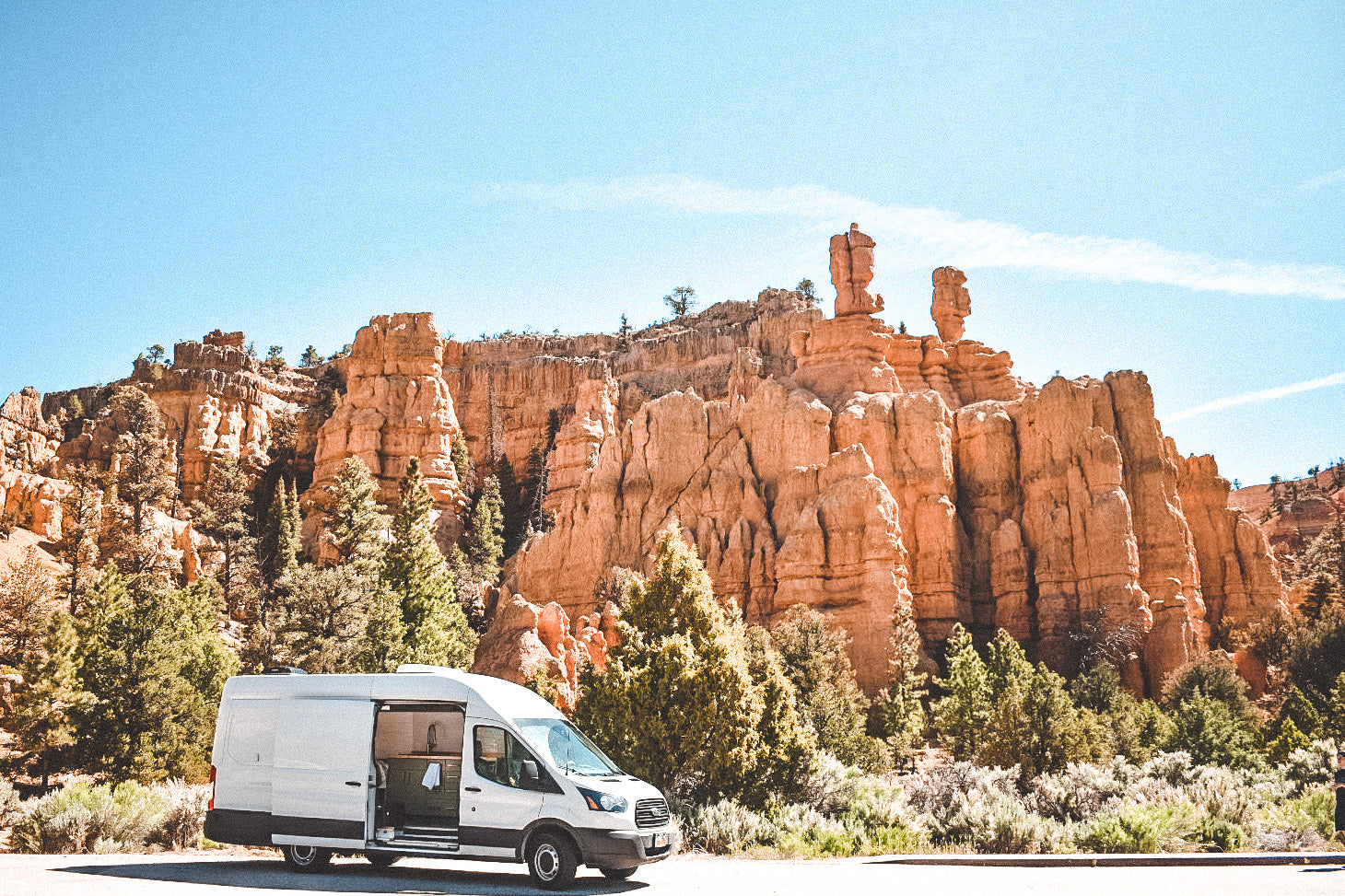 RV rental van at scenic red rock canyon under blue sky with trees. Ideal for adventure & van life.