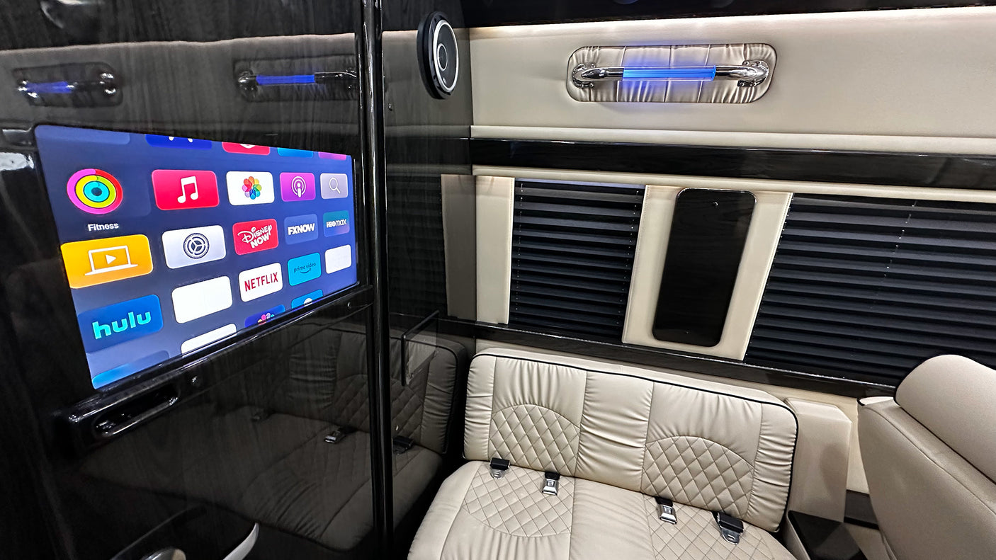 A premium RV rental interior featuring a large smart TV displaying streaming apps, plush quilted seating, and sleek finishes.