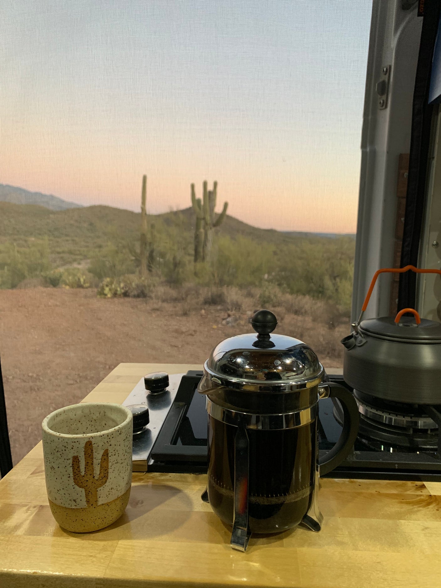 RV rental breakfast setup: French press coffee, kettle, and cactus mug overlooking a stunning saguaro desert sunrise.