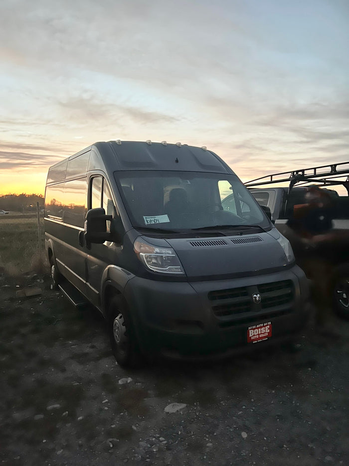 Dark gray Ram ProMaster van from Boise Auto Sales, perfect for rv rental. Parked at sunset with sky reflection.