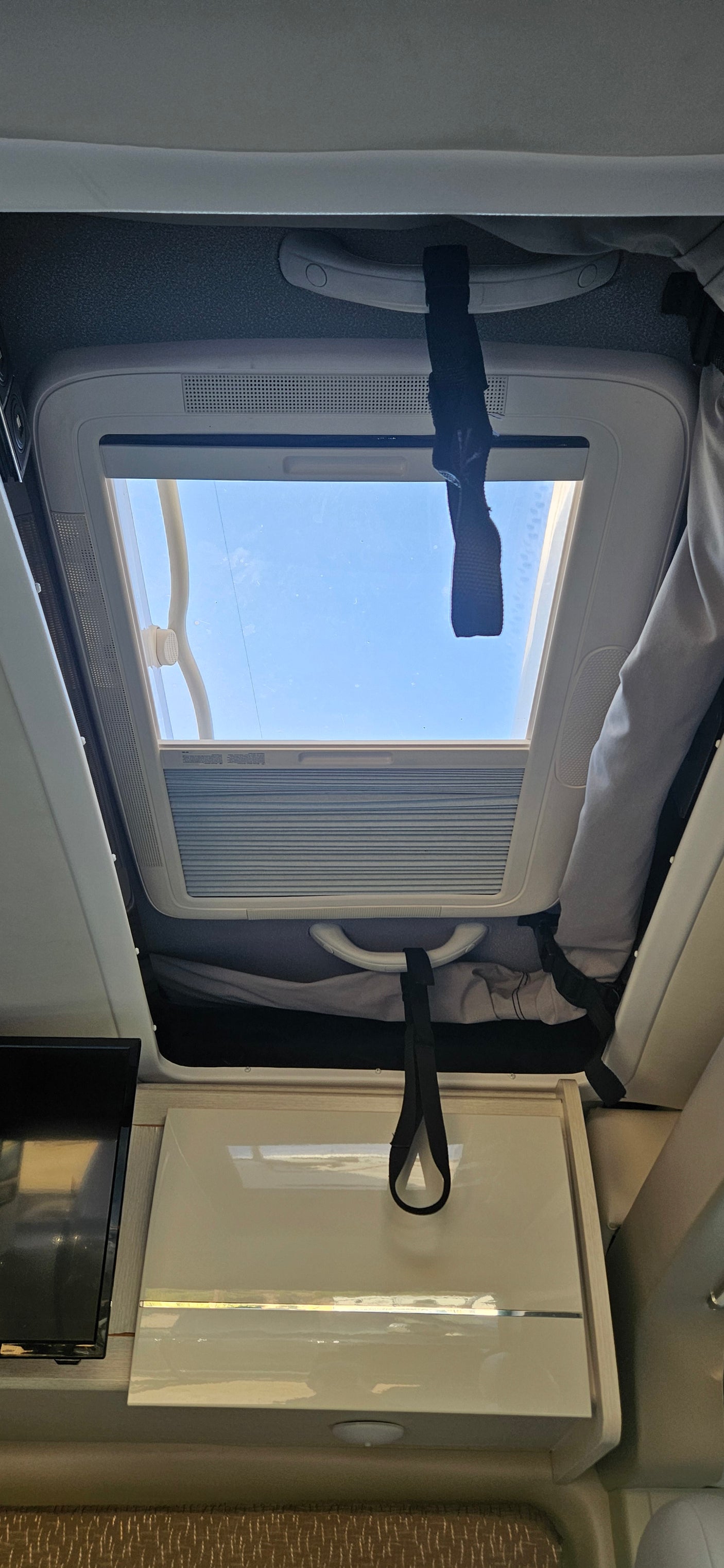 Inside an RV rental: Enjoy the view through the roof skylight. Features include overhead cabinets & a TV, perfect for travel.
