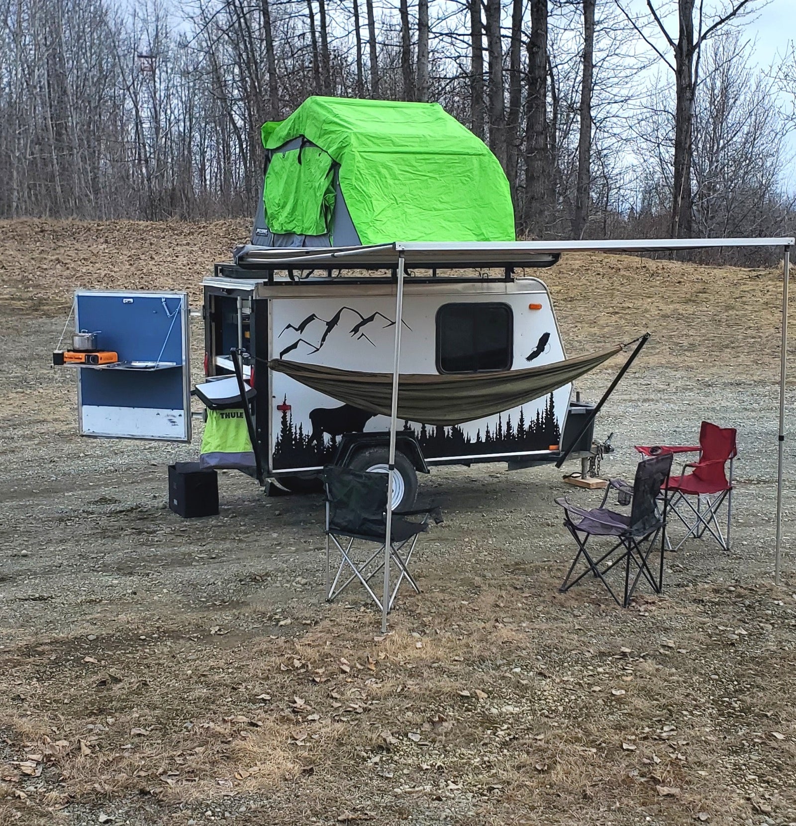 Compact RV rental ready for adventure, with rooftop tent, outdoor kitchen, and chairs for a cozy camp setup.