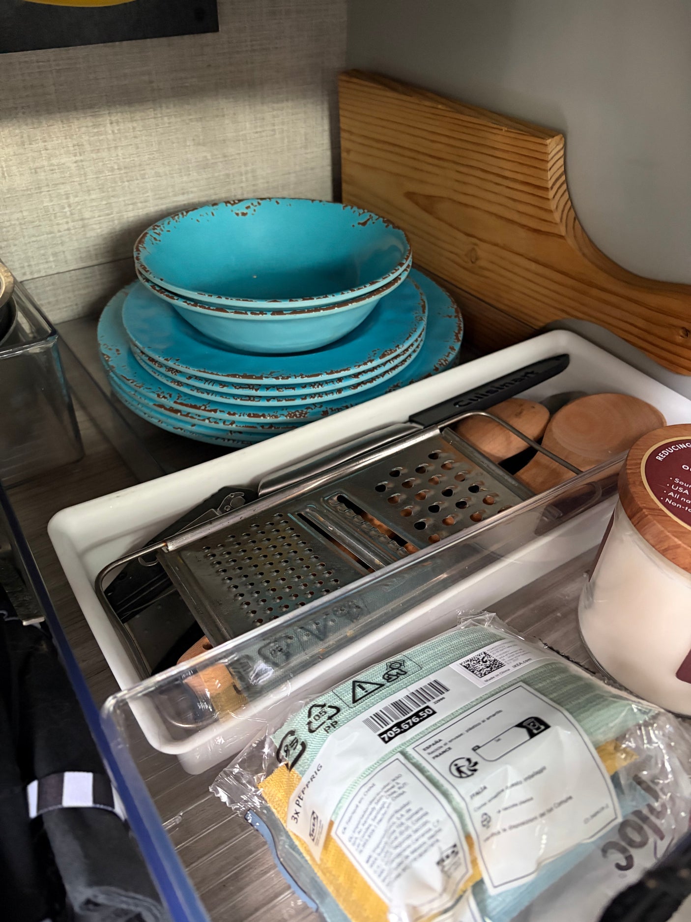 An organized rv rental kitchen with blue dishes, a Cuisinart grater, wooden utensils, and IKEA cloths, neatly stored.