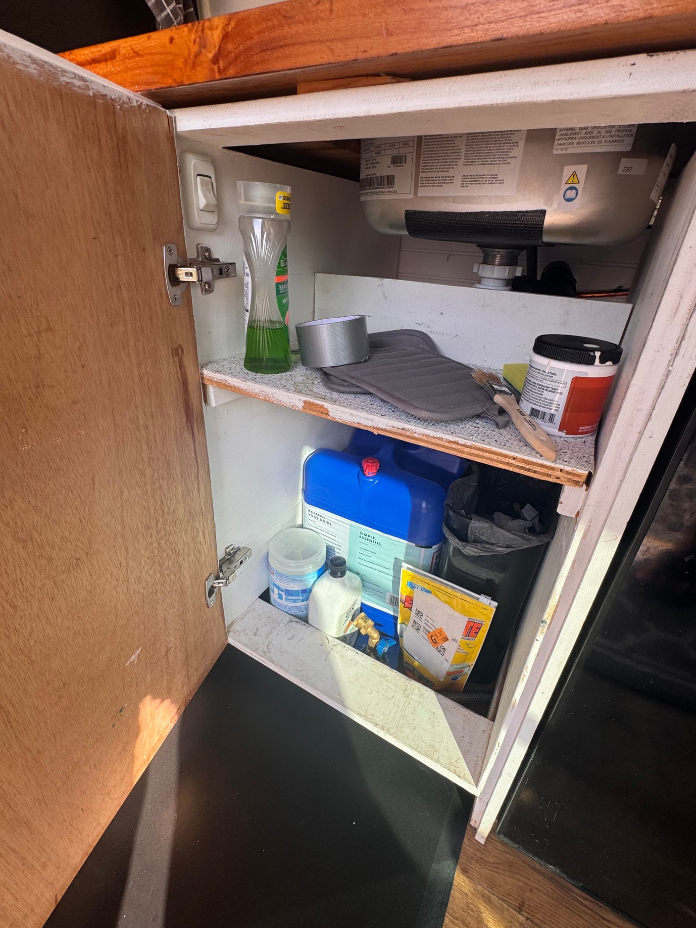 An RV rental's open under-counter cabinet holds cleaning supplies, water jugs, and other essential utility items.
