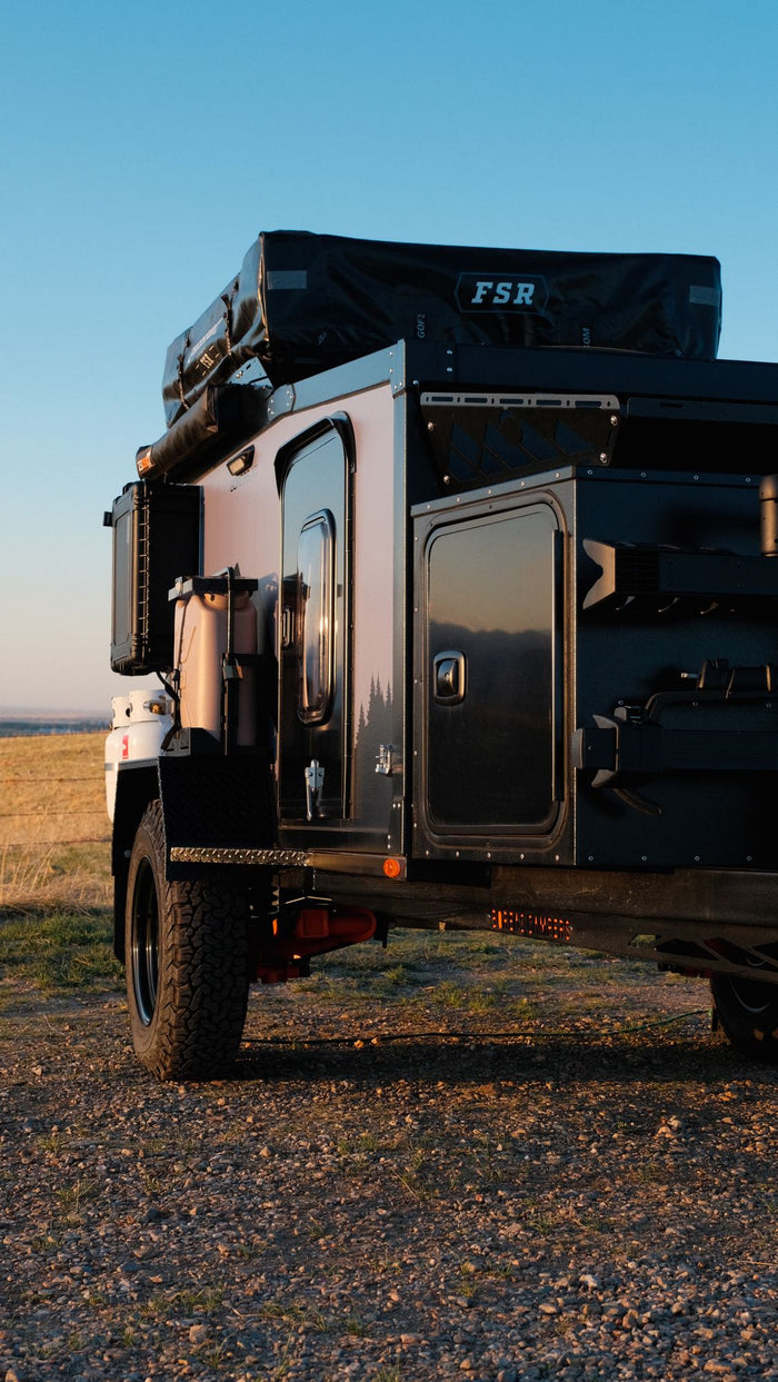 parked on a dirt path with mountains in the background. Perfect for an RV rental adventure.|Rugged off-road camper trailer with a roof tent