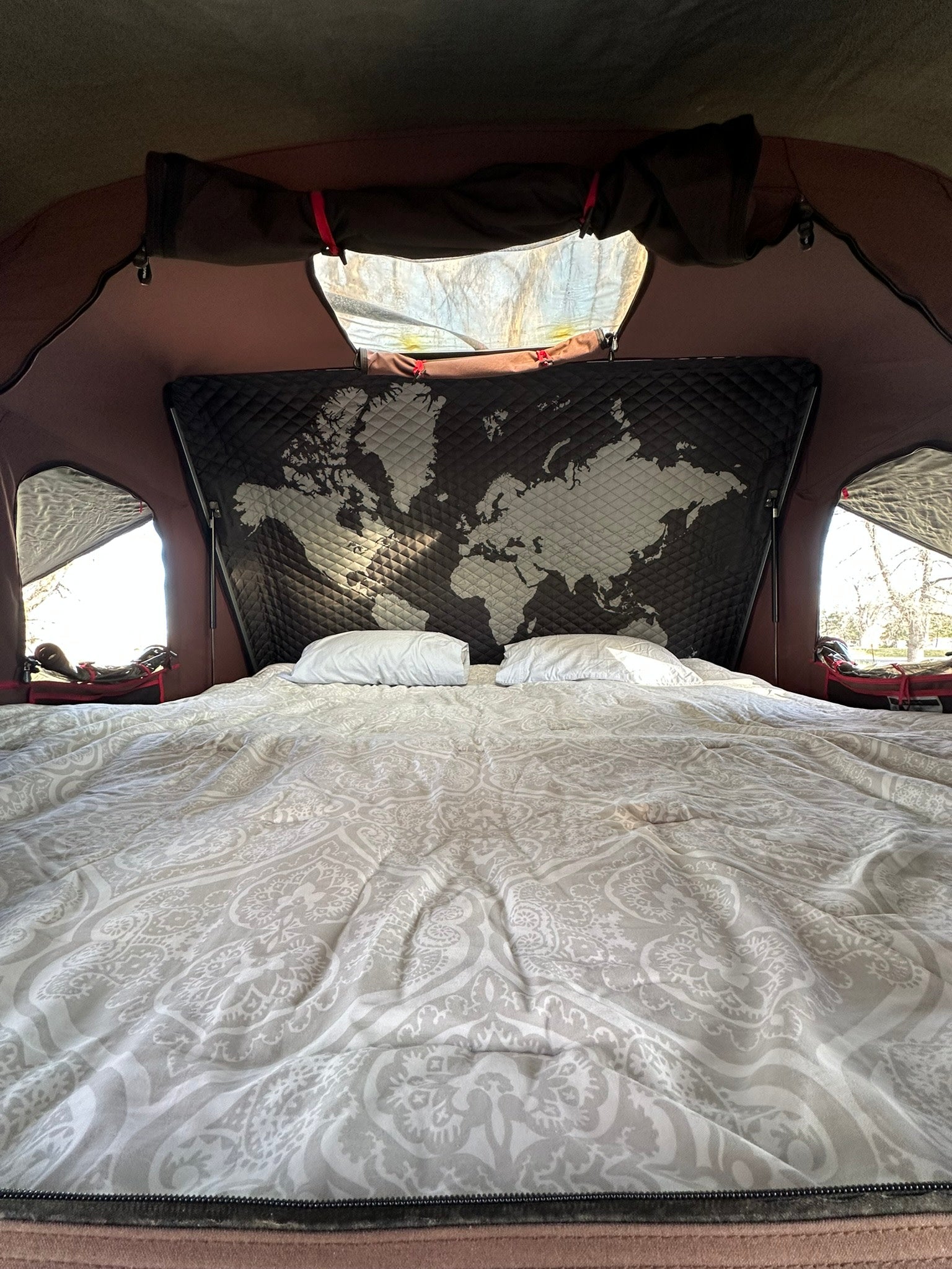 Comfortable bed in an RV rental, featuring a unique world map headboard and bright window views.
