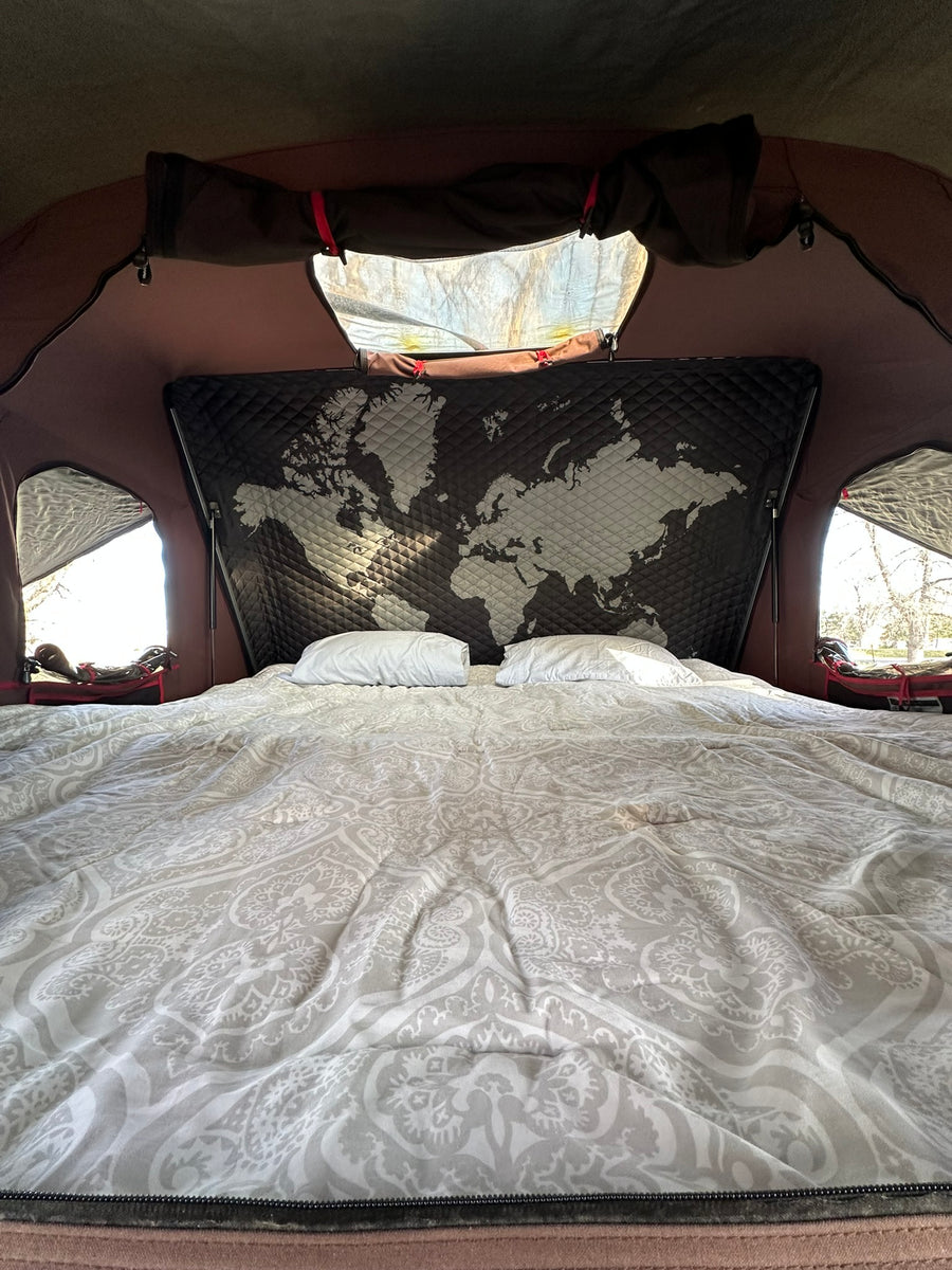Comfortable bed in an RV rental, featuring a unique world map headboard and bright window views.