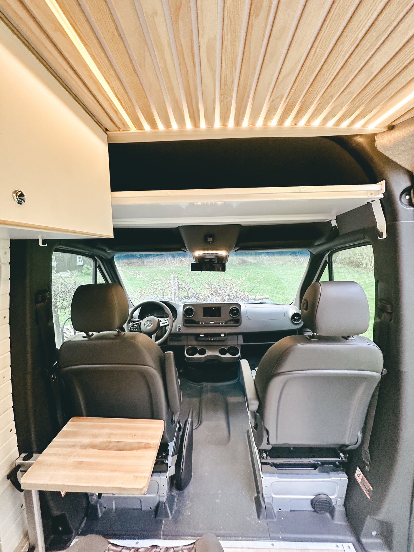 RV rental: Inside a modern camper van looking to the front. Features a warm wooden slatted ceiling with lights, front cabin, and swivel table.