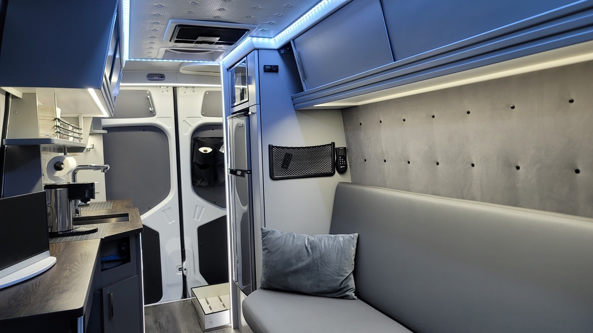 Step inside this sleek RV rental! Enjoy a compact kitchen, fridge, and cozy bench seating with overhead storage for your adventure.