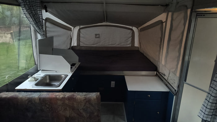 Cozy pop-up RV rental interior, with a bed, sink, and bright window for outdoor adventures.