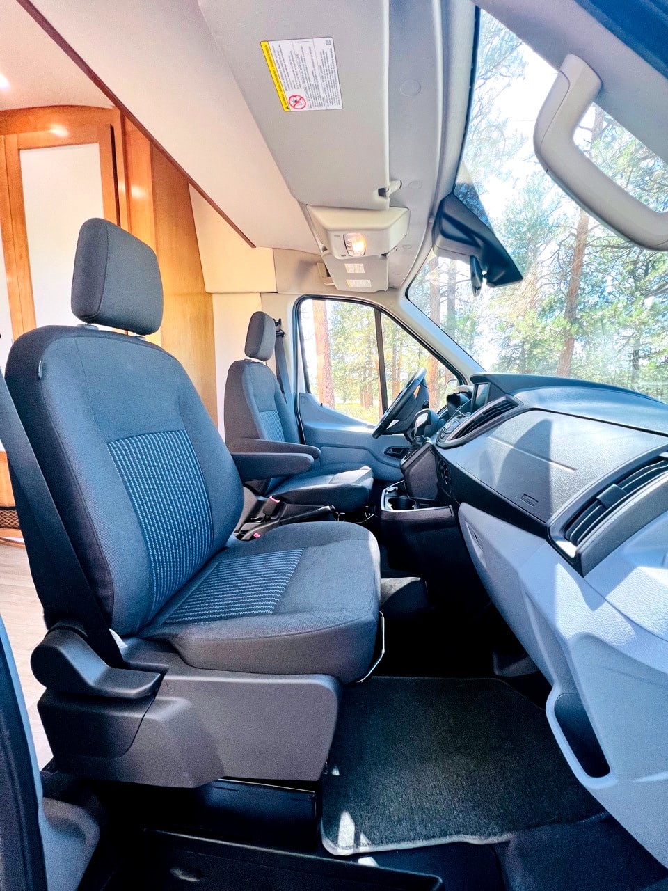 Comfortable RV rental interior with front seats, dashboard, and a clear forest view, ideal for adventures. — photo 5