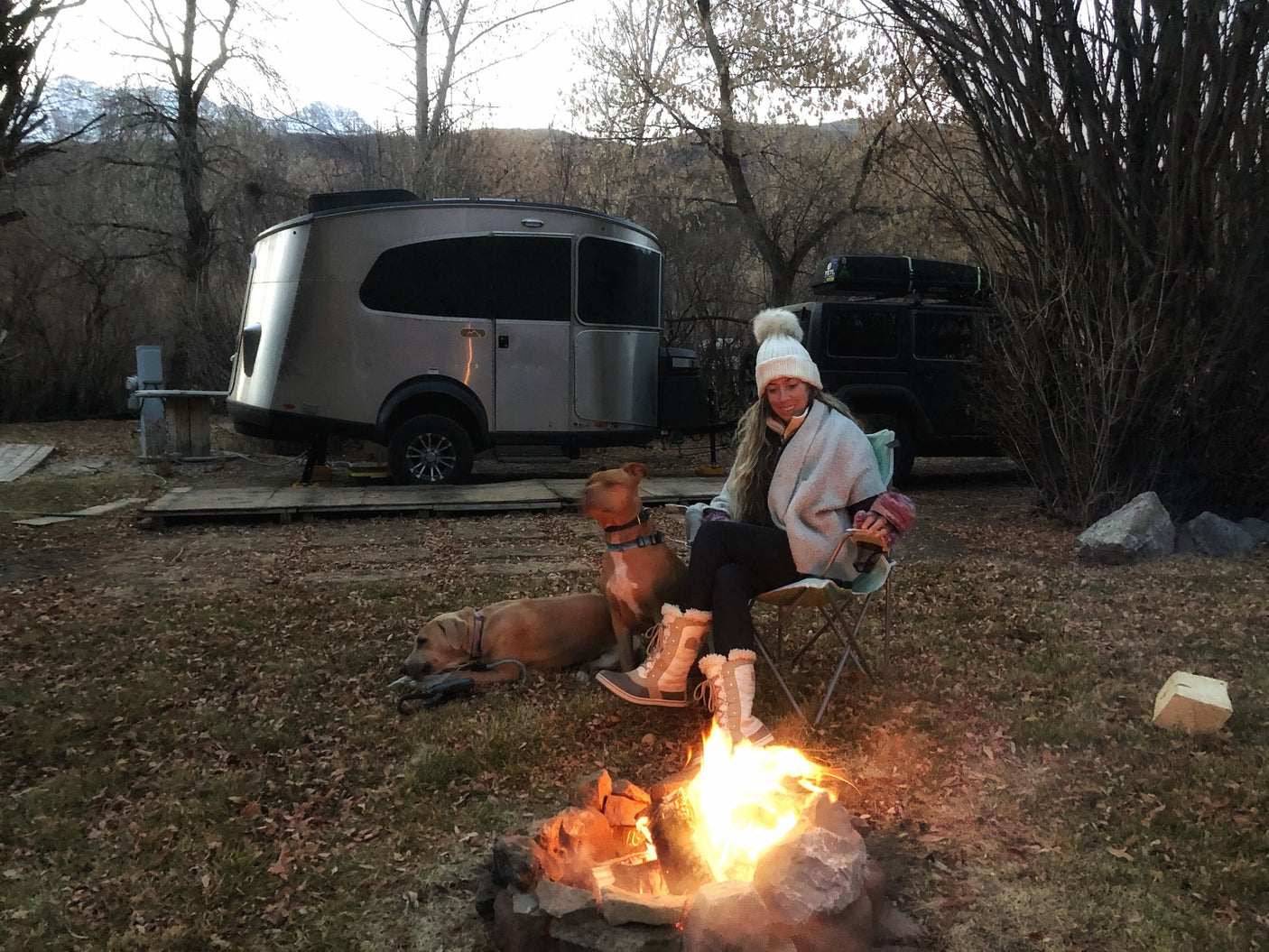 surrounded by stunning desert rock formations under a clear blue sky.||Camping bliss! A person and two dogs by a campfire