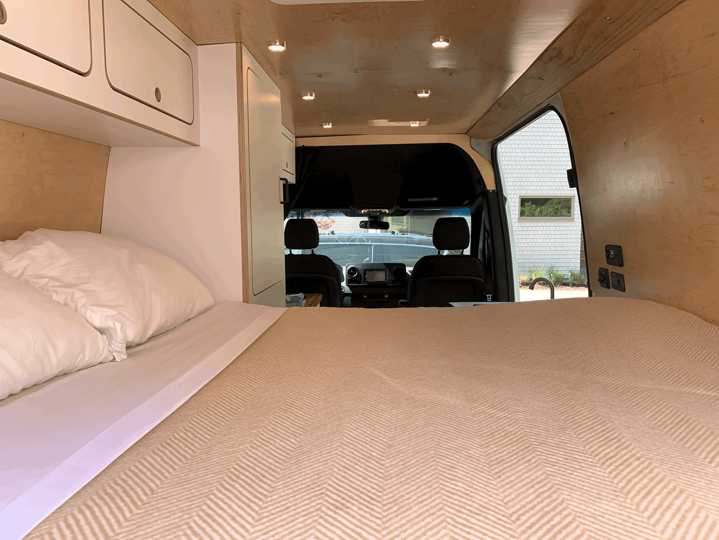 Cozy RV rental interior featuring a comfortable bed, overhead cabinets, warm wooden paneling, and the driver's cab.