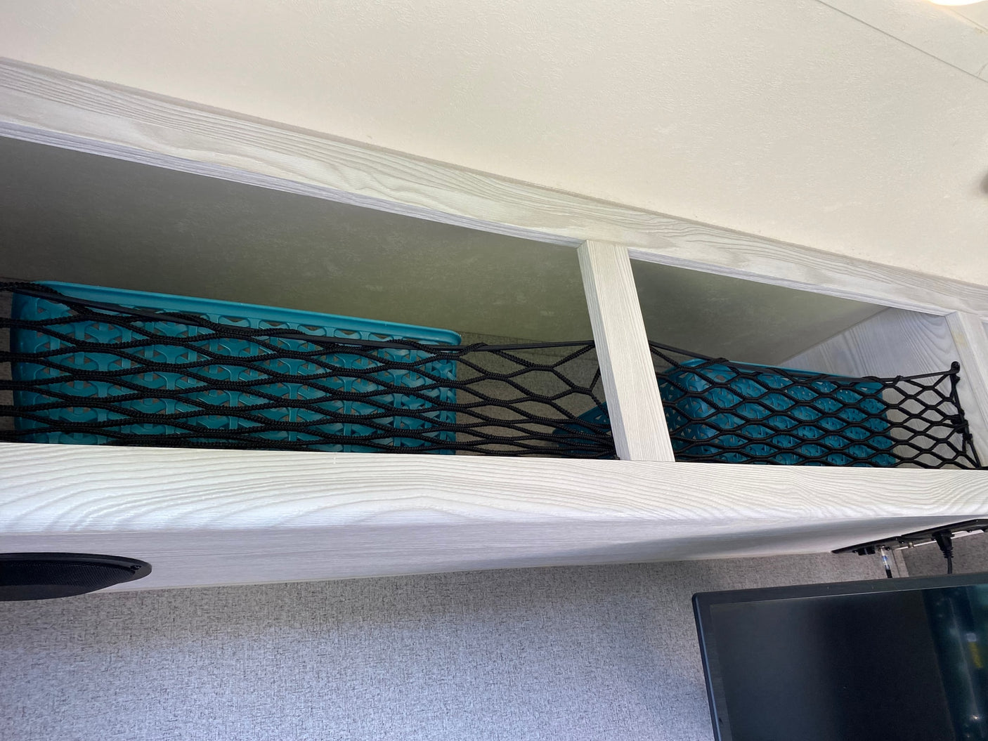 RV rental: Secure overhead storage in this RV, featuring blue bins and a black mesh net for organizing items.
