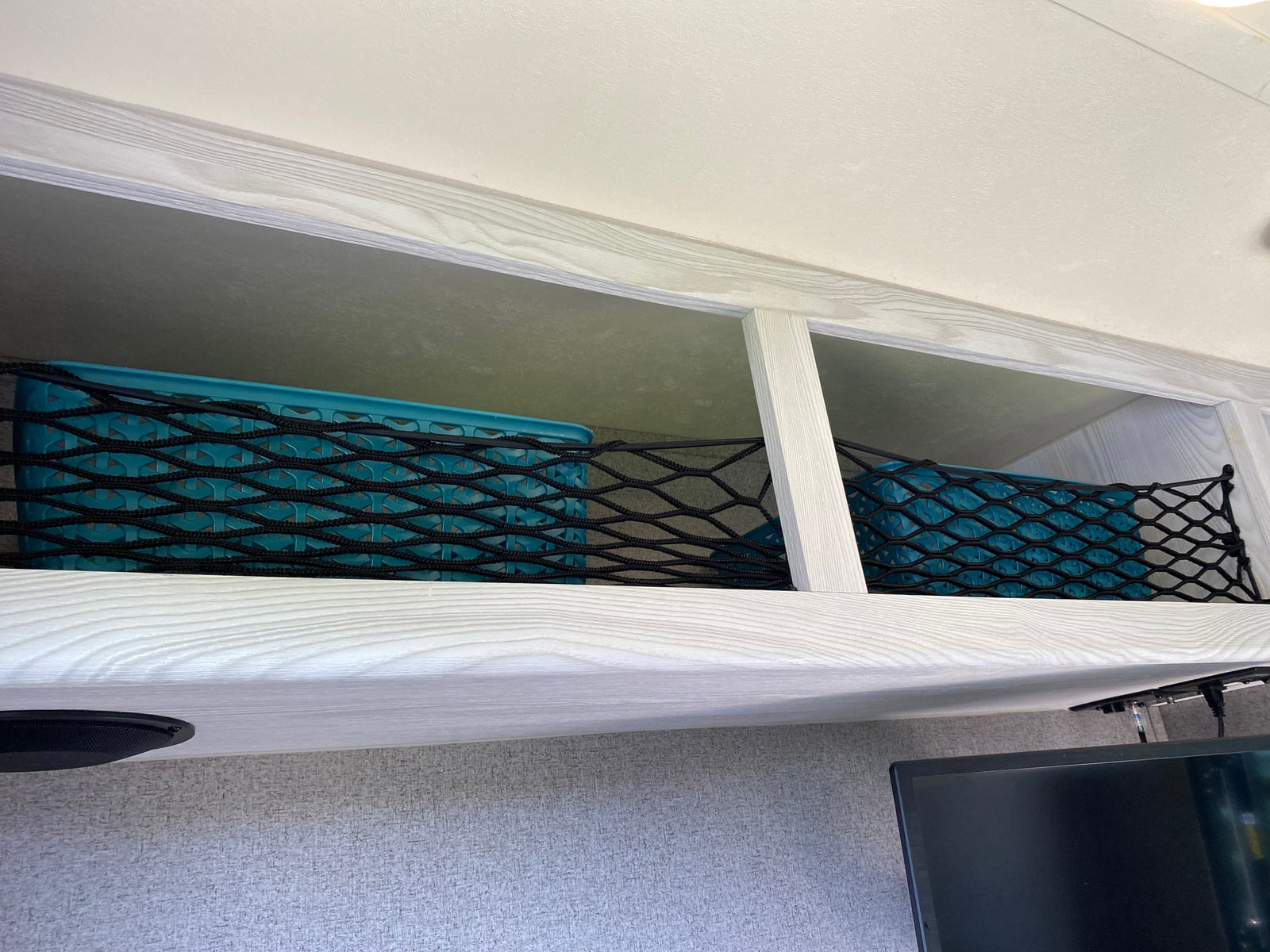 RV rental: Secure overhead storage in this RV, featuring blue bins and a black mesh net for organizing items.