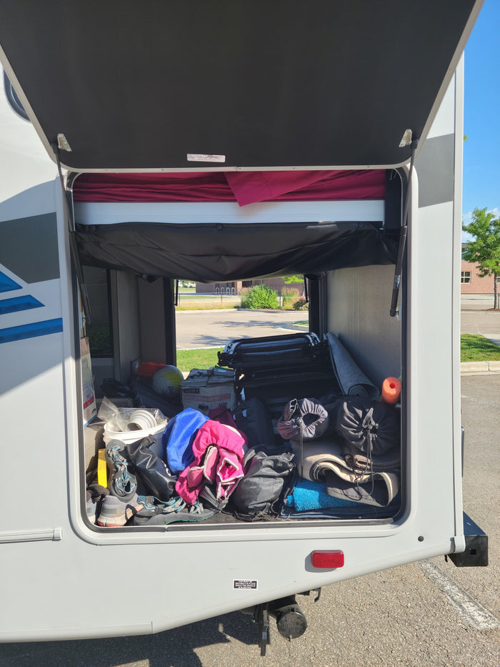 An rv rental's rear storage 'garage' is open, revealing it fully packed with diverse camping and travel gear.