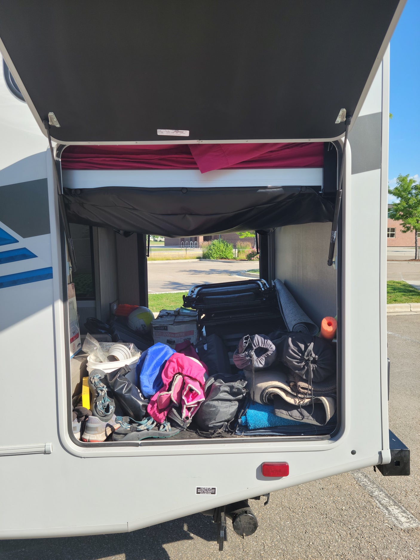 An rv rental's rear storage 'garage' is open, revealing it fully packed with diverse camping and travel gear.