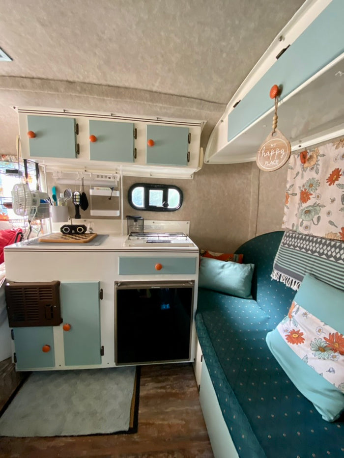 and rustic wood-look flooring.|Open RV rental door reveals a floral curtain and cozy interior with wood floors.|Step inside this cozy rv rental! It features a compact kitchen