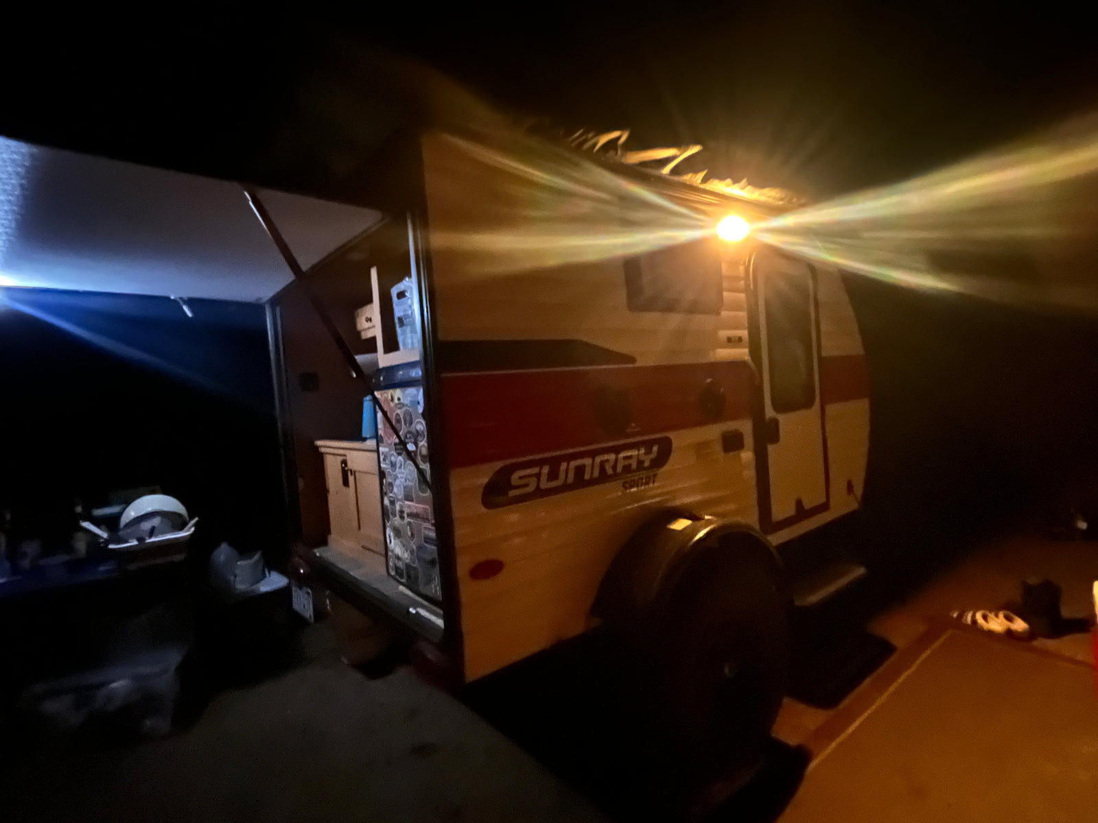 Illuminated Sunray Sport rv rental at night, with an open rear galley kitchen and extended awning. Ideal for travel and camping.