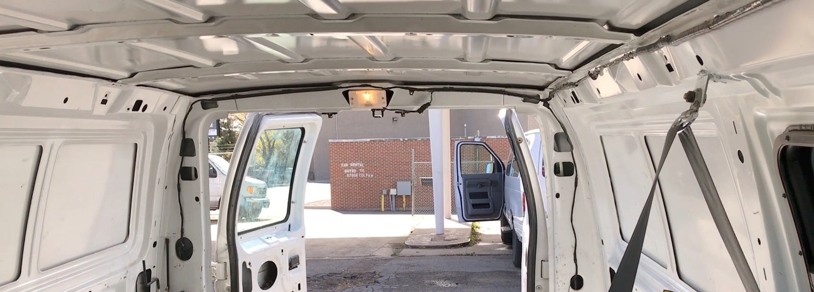 Inside a spacious white rental van, doors open, showing the unpaneled interior—perfect for an RV rental build.