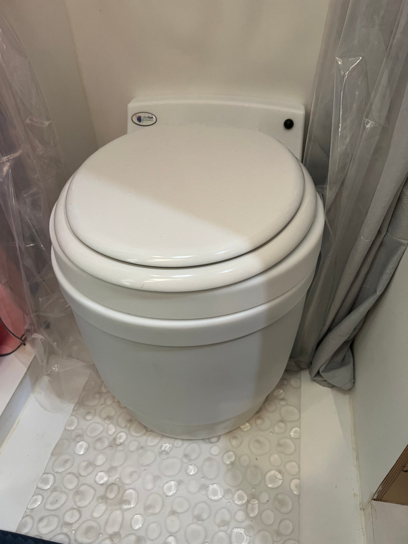 A compact white DryFlush toilet with its lid closed, set on a unique bubble-textured floor in an RV rental bathroom.