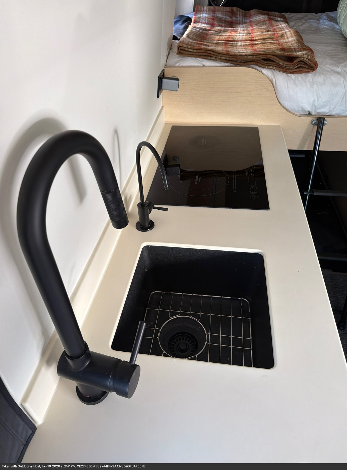 Modern RV rental kitchen with black sink, gooseneck faucet, water filter, and Furrion induction cooktop.