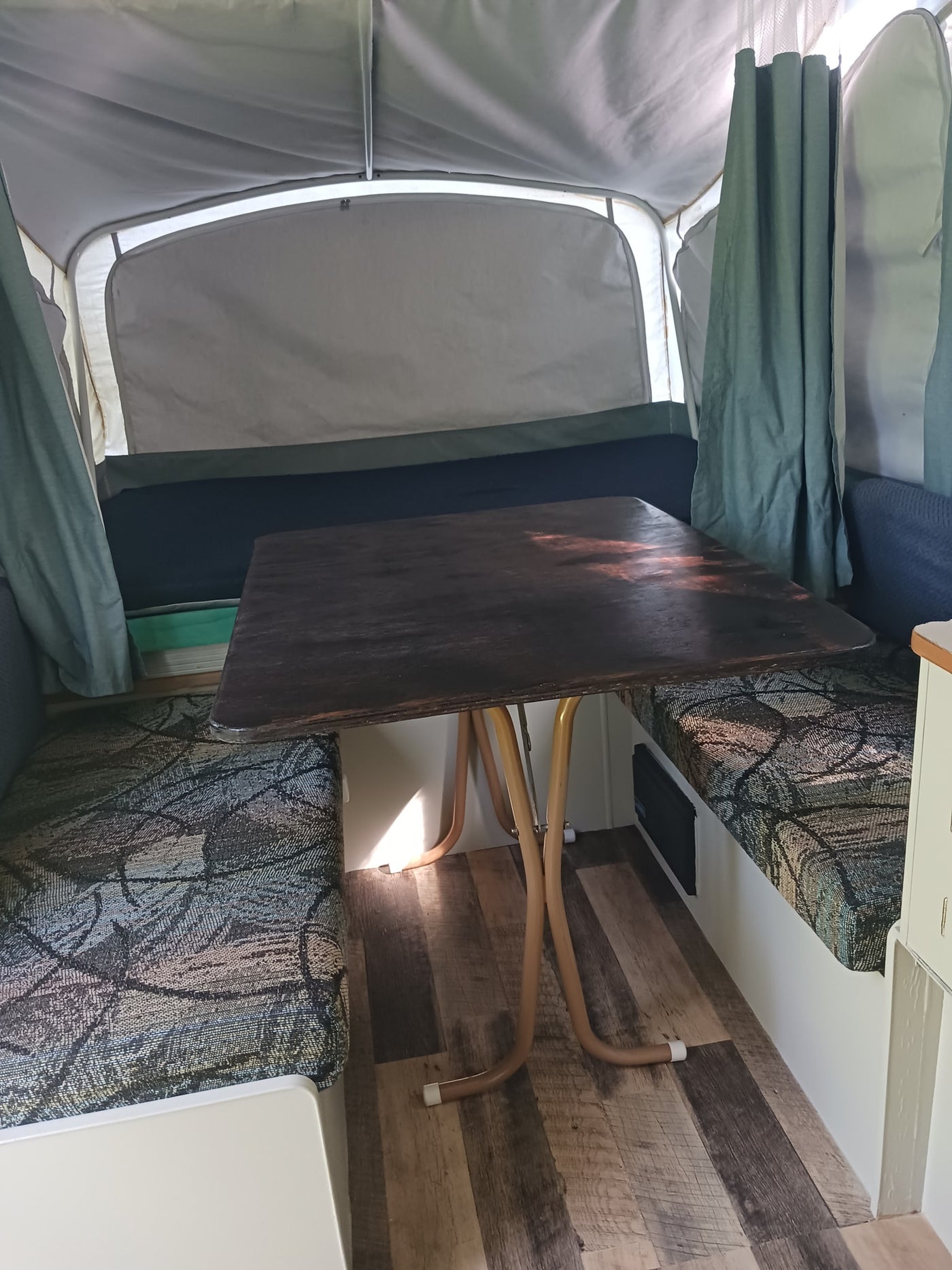 RV rental: Inside a pop-up camper featuring a dark wooden table, patterned benches, and light fabric walls. — photo 6