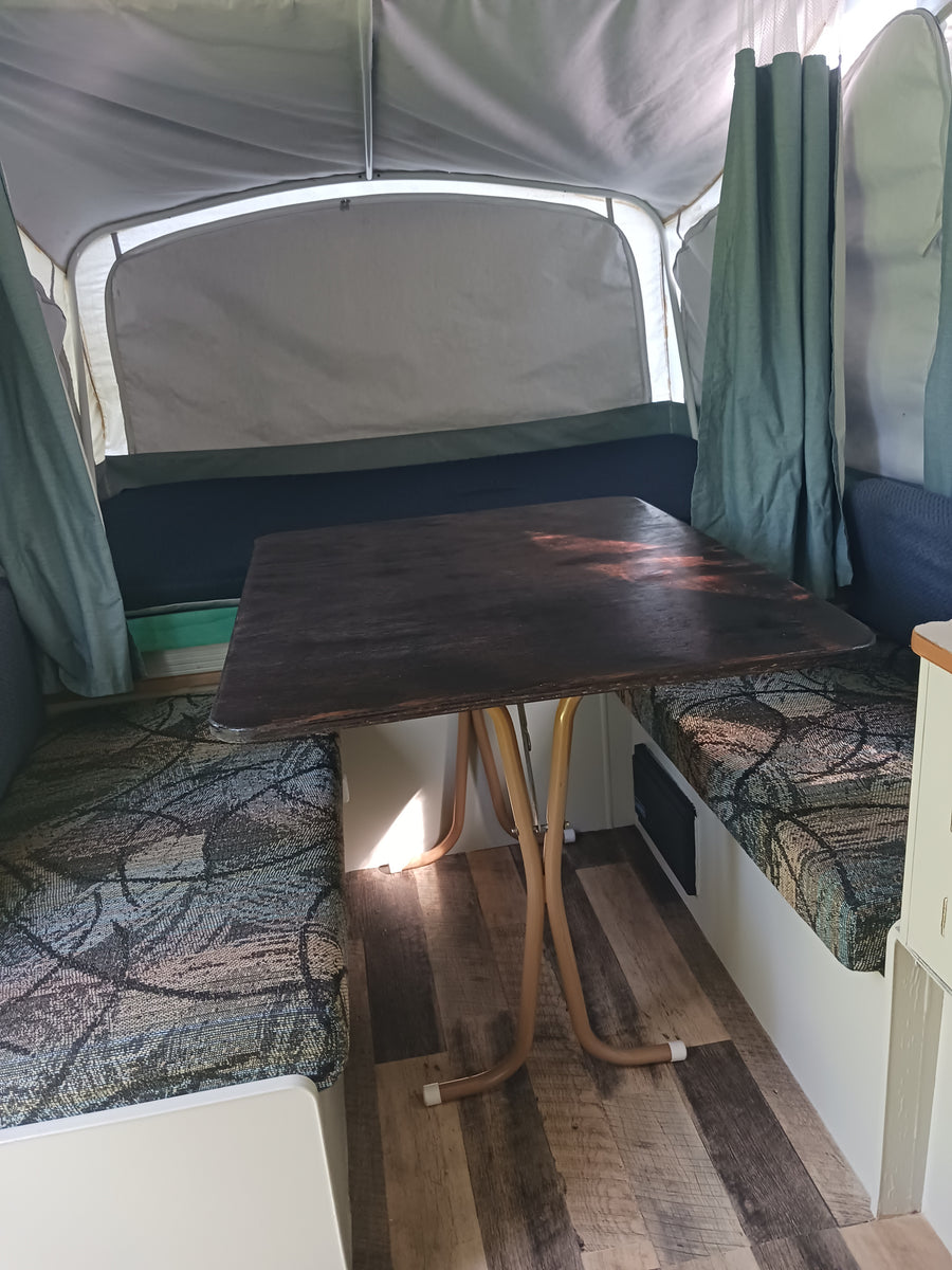 RV rental: Inside a pop-up camper featuring a dark wooden table, patterned benches, and light fabric walls.