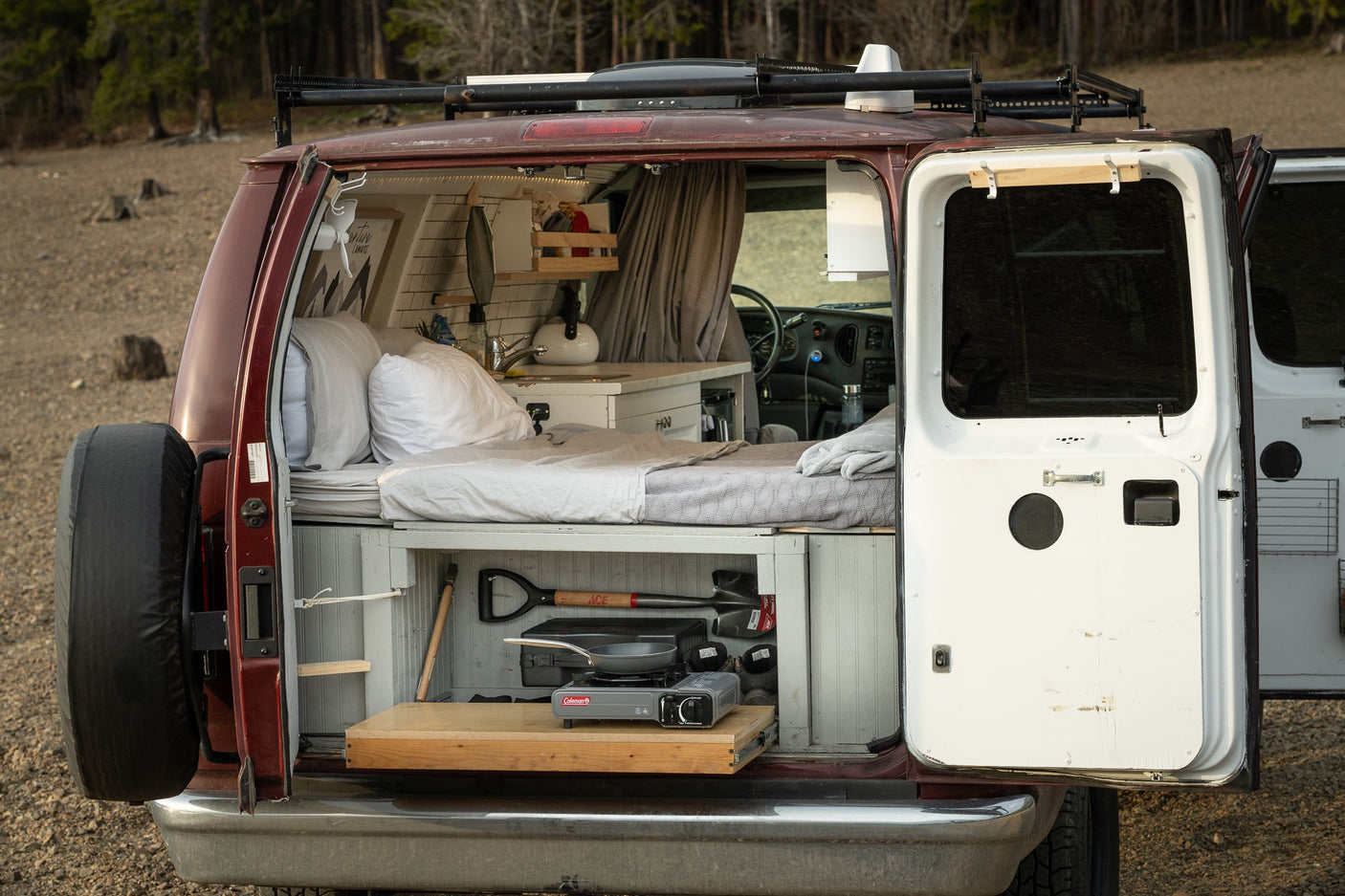 Inside this custom camper van, ideal for RV rental, a bed, kitchen, and pull-out stove are visible.