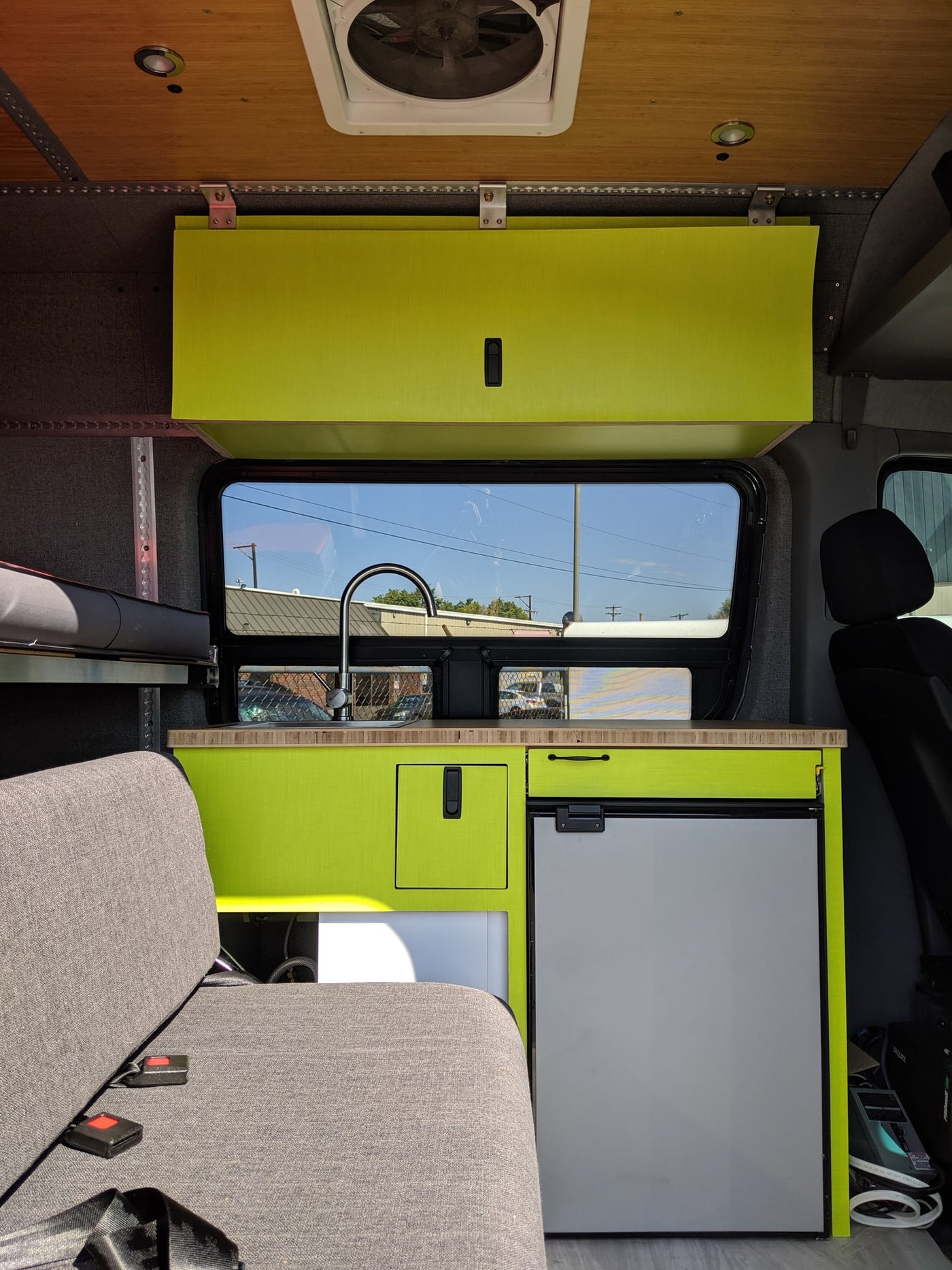Vibrant lime green cabinetry and kitchenette with sink, fridge, and seating inside a cozy RV rental camper van. — photo 3